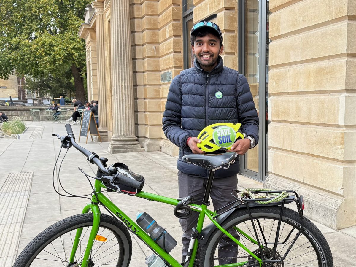Sahil Jha smiling beside his green touring bicycle, holding a Save Soil helmet